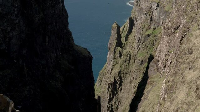 Aerial tilt down shot of gigantic Beinisvord Cliff on Suduroy Island during sunny day