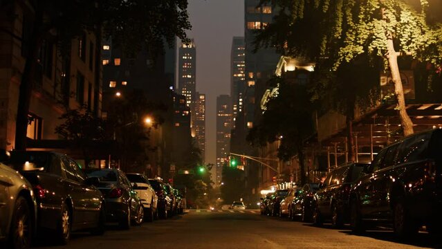 Camera travels down middle of New York City street covered in smoke from wildfires at night. .buildings in background are faded away by smoke.