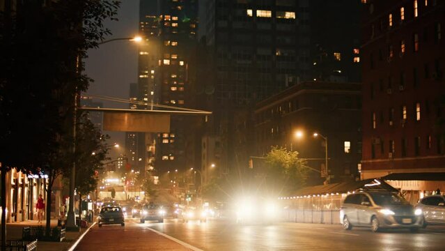 Traffic drives past camera in a smoke covered New York City  at night. buildings in background are faded away by smoke.