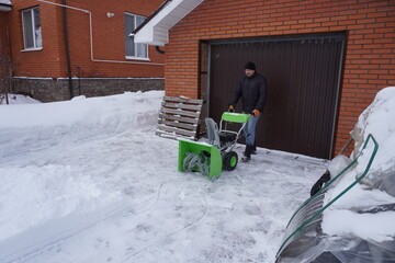A man cleans snow in the winter in the courtyard of the house,  man cleaning snow with a snow blower