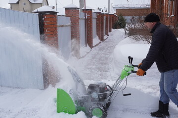 A man cleans snow in the winter in the courtyard of the house,  man cleaning snow with a snow blower