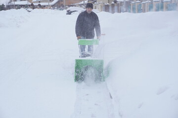 A man cleans snow in the winter in the courtyard of the house,  man cleaning snow with a snow blower