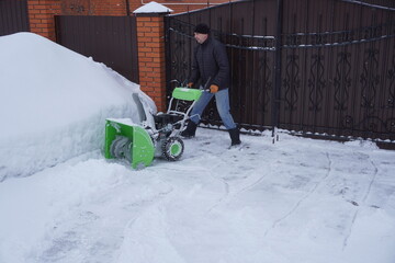 A man cleans snow in the winter in the courtyard of the house,  man cleaning snow with a snow blower
