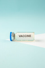 Vertical view of COVID- VACCINE in a fallen ampoule on pastel blue background with free space