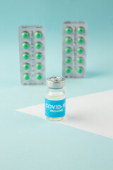 Vertical view of vaccine in medical ampoule packed green pills for Covid- treatment on pastel blue background