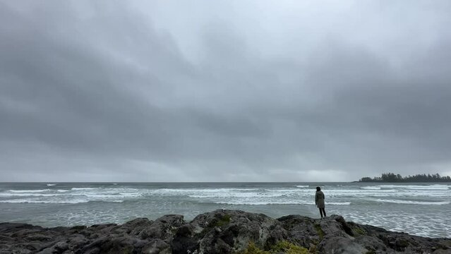 Person standing with an umbrella on rocky shoreline staring at the ocean as waves crashes on shore, near Tofino, British Columbia