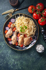 Vertical view of raw pastas chickens and vegetables on a plate and cutlery set tomatoes spices wooden hammer cutlery set on green black mix colors background