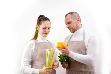 Obraz na płótnie Canvas husband wife in kitchen aprons look at vegetables people's clothes background are white they have peppers their hands celery parsley cilantro they are vegetarians fresh vegetables cook dinner 
