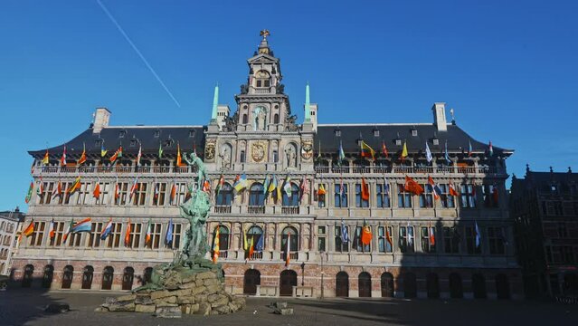 View of Brabo fountain and four-story Renaissance building of Antwerp City Hall with main facade lavishly decorated with sculptures and waving flags located on central Grote Markt square, Belgium 