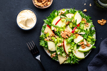 Waldorf salad with red and green apple, raw celery, lettuce, arugula and walnuts with mayonnaise dressing, black table background, top view