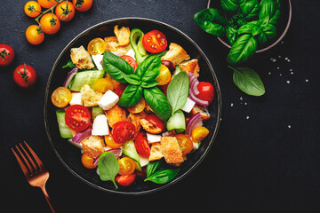 Panzanella salad with stale bread, colorful tomatoes, mozzarella cheese, onion, olive oil, salt and green basil, black table background, top view