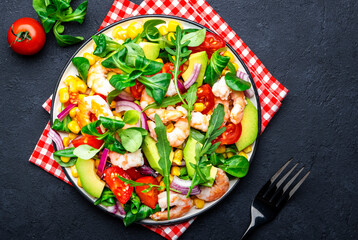 Fresh salad with shrimps, sweet corn, avocado, red tomatoes, lamb lettuce and onion on black table background. Top view