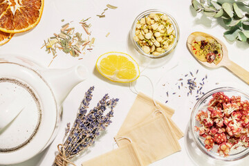 Organic healing tea from wild plants and flowers. Home herbal apothecary concept. Sustainable still life with dry flowers and herbs, lemon, paper tea bags, teapot and wooden spoon on white background