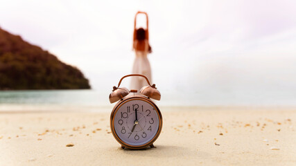 Alarm clock on the bech with woman playing yoga and stretching muscles on the beach sunlight in morning. Health concept.