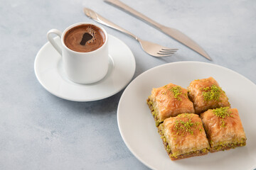 Pistachio baklava on a white plate with Turkish coffee.A plate of traditional baklava on light blue background
