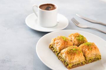 Pistachio baklava on a white plate with Turkish coffee.A plate of traditional baklava on light blue background
