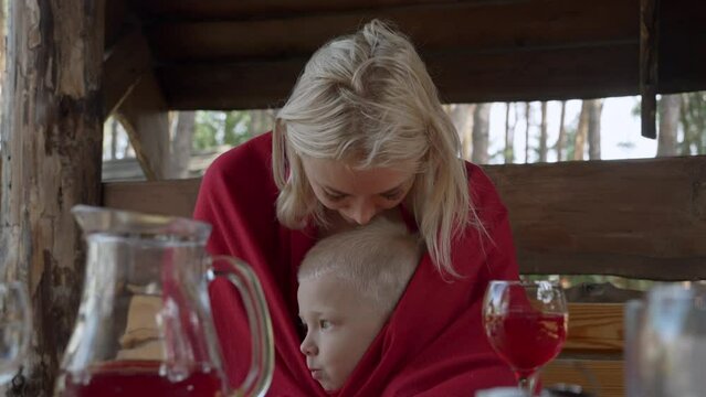 A young mother hugs and gently kisses her little son during breakfast in a cafe in nature. A woman shows love and care for her child. The concept of a happy family with one parent. Healthy lifestyle.