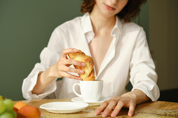 Woman dipping croissant into cappuccino at home