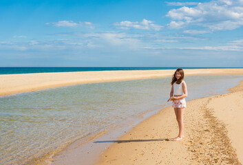 Fototapeta na wymiar Beautiful fashionable young girl walking on the beach barefoot 
