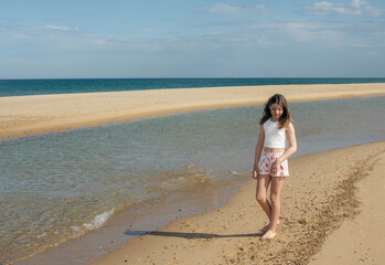 Beautiful fashionable young girl walking on the beach barefoot 