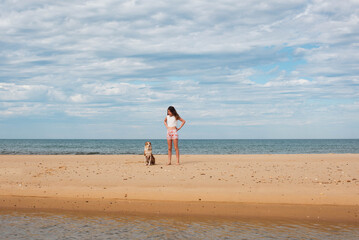 Beautiful fashionable young girl having fun on the beach barefoot with her dog