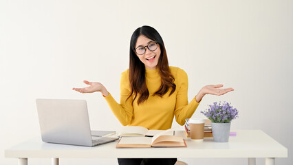 A smiling Asian female college student in glasses opens her palms while sitting at her desk
