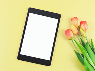 flat lay of digital tablet with blank white screen, tuip flowers  isolated on yellow background.