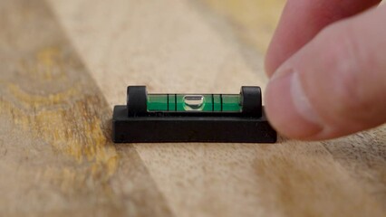 Engineer hand puts mini tool spirit level with green liquid and bubble on wood surface
