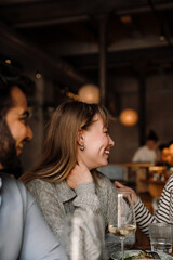 Portrait of cheerful woman drinking wine and talking with friends while sitting in restaurant