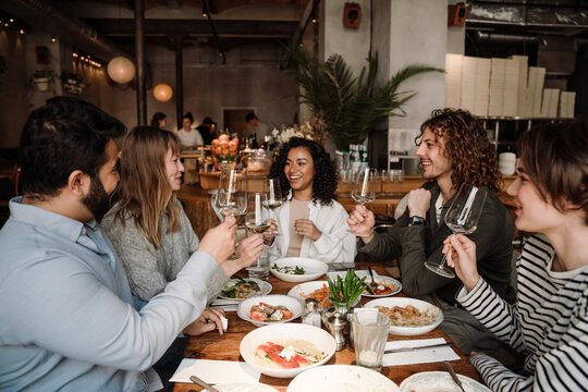 Group of joyful friends talking and drinking wine while dining in restaurant