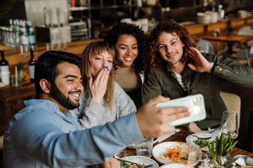 Group of cheerful friends taking selfie while dining in restaurant