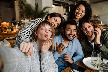 Group of cheerful friends taking selfie while dining in restaurant