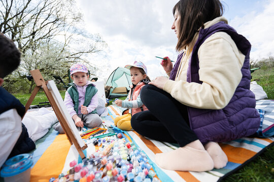Happy young family, mother and children having fun and enjoying outdoor on picnic blanket painting at garden spring park, relaxation.