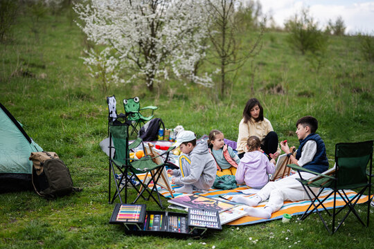 Happy young family, mother and children having fun and enjoying outdoor on picnic blanket painting at garden spring park, relaxation.