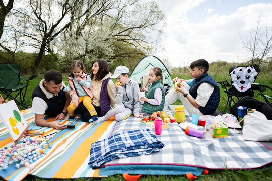 Happy young large family with four children having fun and enjoying outdoor on picnic blanket at garden spring park, relaxation.