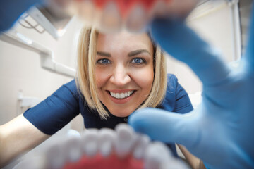 Close-up smiling female dentist examining teeth in clinic in first person. View through the mouth dental checkup.