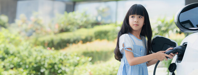 A playful girl holding an EV plug, a home charging station providing a sustainable power source for...
