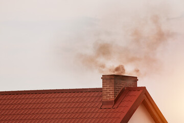 Dark smoke comes out of the chimney of a modern house in winter. Heating with solid fuel. The...