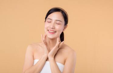 Beautiful girl asian model touching fresh glowing hydrated facial skin on beige background closeup....