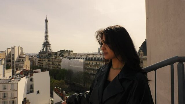 Beautiful young brunette woman standing on a rooftop with the famous Tour Eiffel in the background, in Paris, France