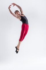 Obraz premium Contemporary Ballet of Young Flexible Athletic Man Posing in Red Tights in Flying Dance Pose With Hands Connected in Studio on White.