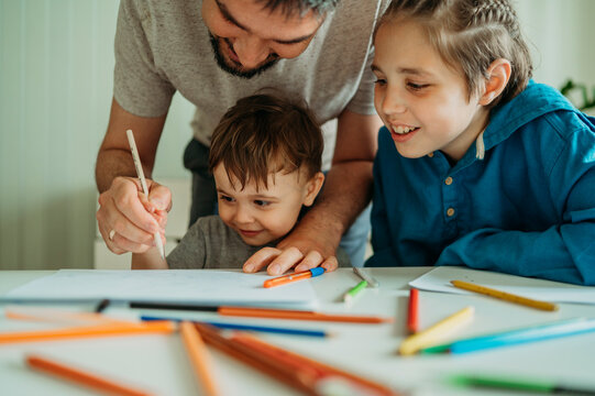 Smiling father teaching sons to draw using pencil at home