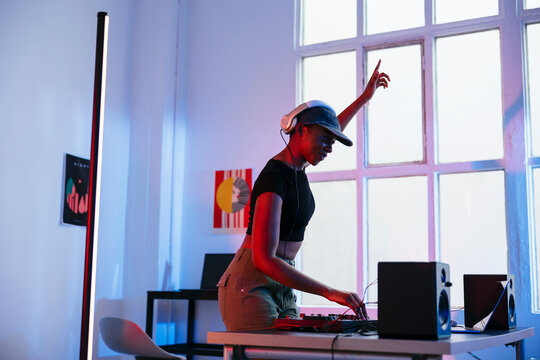 Smiling young DJ with arm raised operating sound mixer