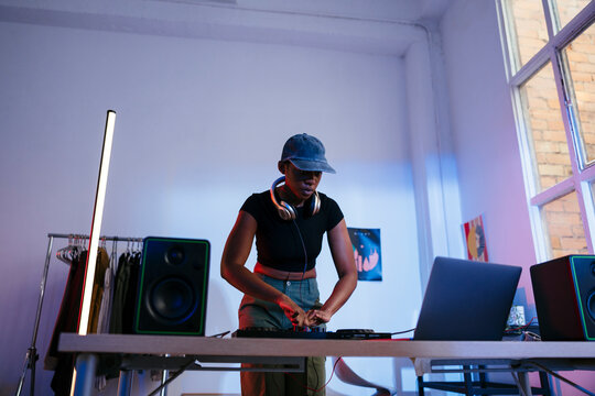 Young Dj using laptop and operating sound mixer at home