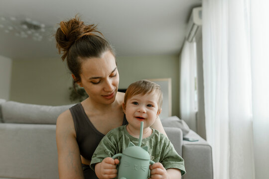Mother sitting with daughter holding sipper bottle at home