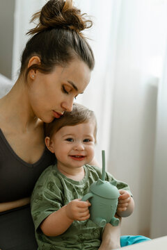 Mother looking at smiling daughter holding sipper bottle at home