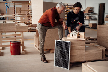 Senior businessman having discussion over model home with colleague in workshop