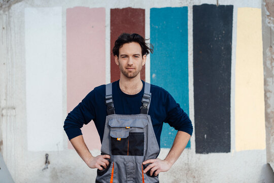 Carpenter with arms akimbo standing in front of multi colored wall