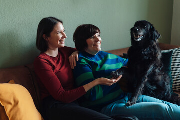 Smiling lesbian couple playing with dog at home