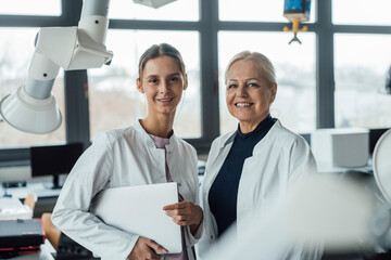 Happy scientists standing together by robotic arm in laboratory